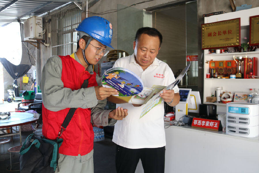图为“电力小黄车”向商铺老板进行安全用电及防火知识宣传（梁梦 摄）