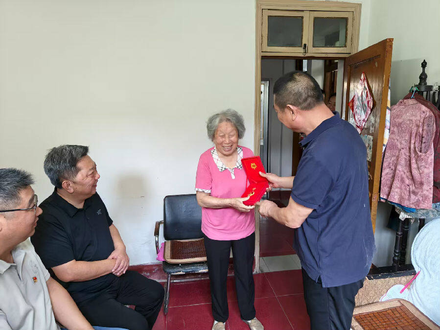 新安镇镇东社区党总支书记陈德军向常学荣递上“光荣在党50年”纪念章（嵇曼曼 摄）